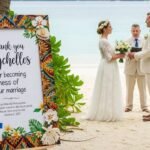Finnish couple getting married on a Seychelles beach with an invitation board reading “Thank you Seychelles for becoming witness of our marriage.